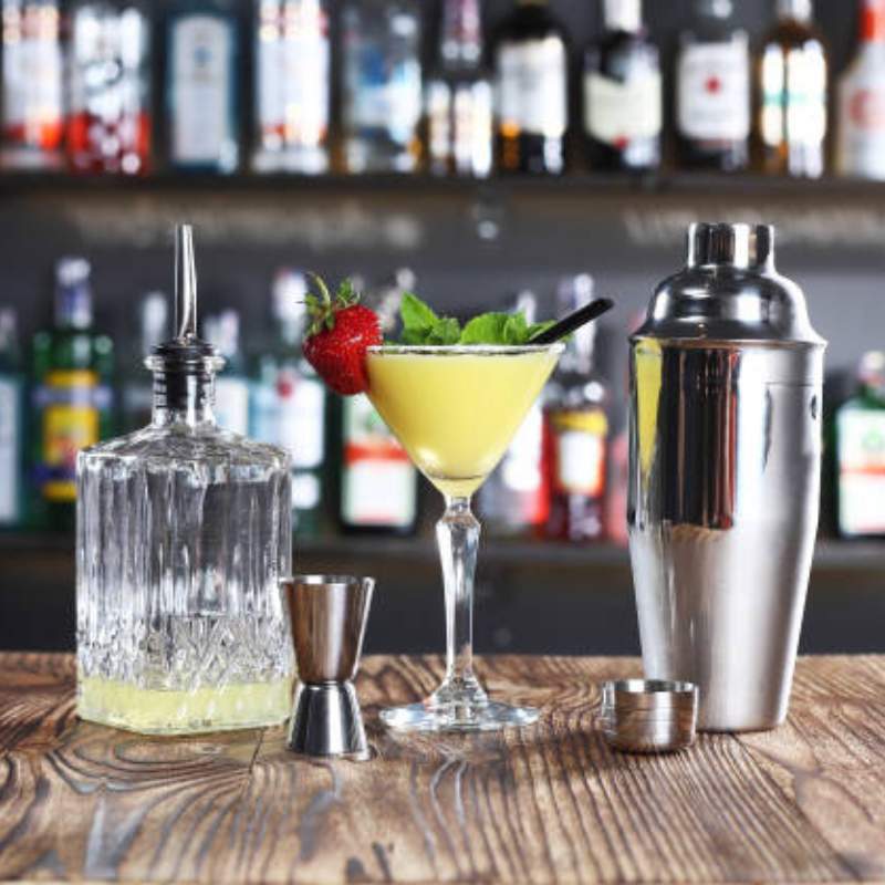 A wooden table features a cocktail shaker and glass, perfect for making delicious cocktails at home.