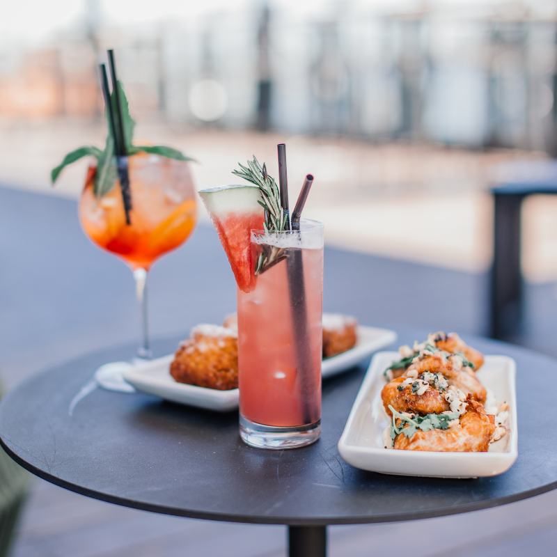 A lively table showcasing a variety of cocktails and mocktails alongside an array of delicious food.