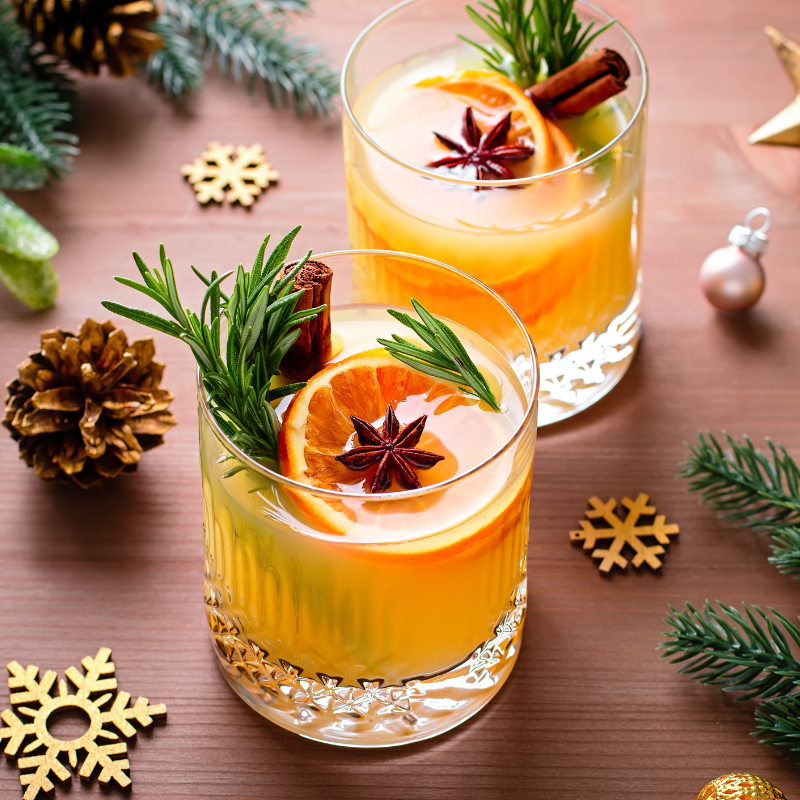 Two glasses of orange beverage with festive garnishes, surrounded by cheerful Christmas decorations for a cozy holiday atmosphere.