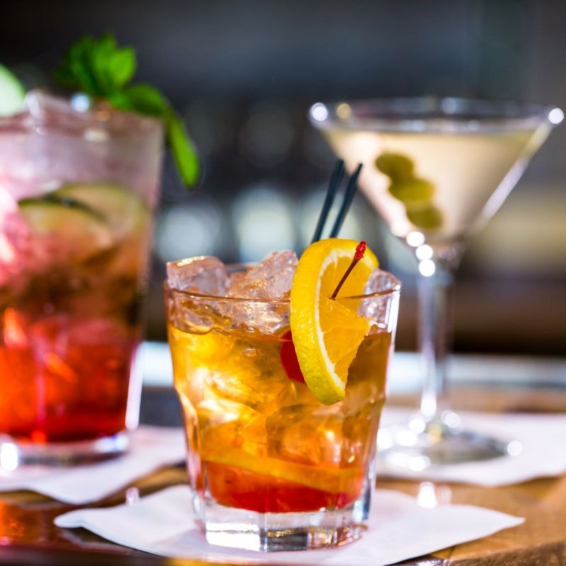 Three different cocktails displayed on a bar, each with unique colors and garnishes, ready to enjoy.