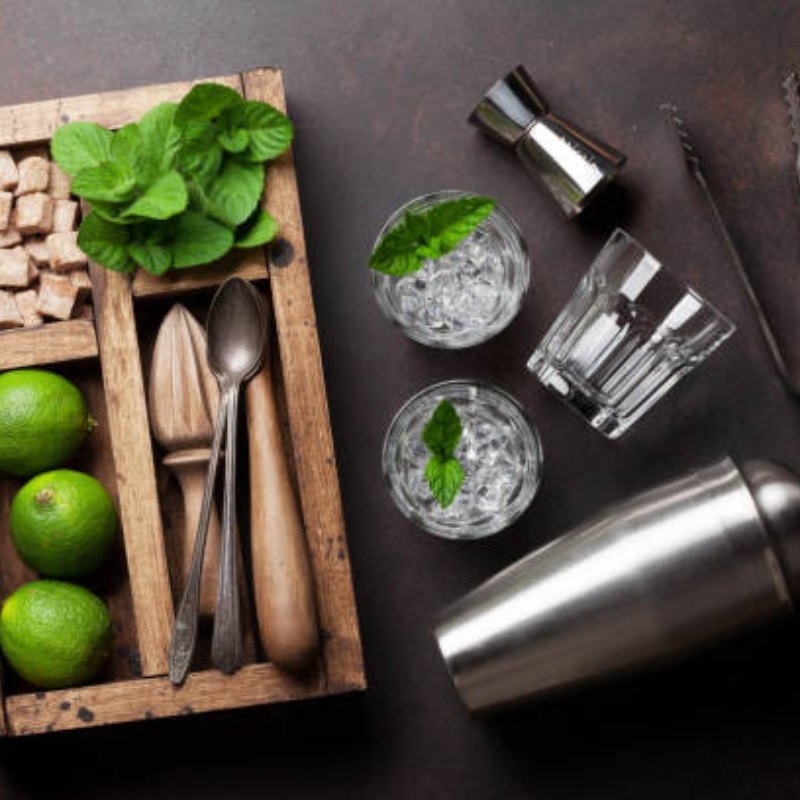 A wooden tray with cocktail making tools and glass, lime and mint.